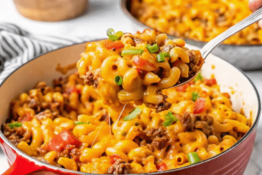 Cheesy beef macaroni skillet in a red pot with a spoonful lifted, topped with chopped green onions